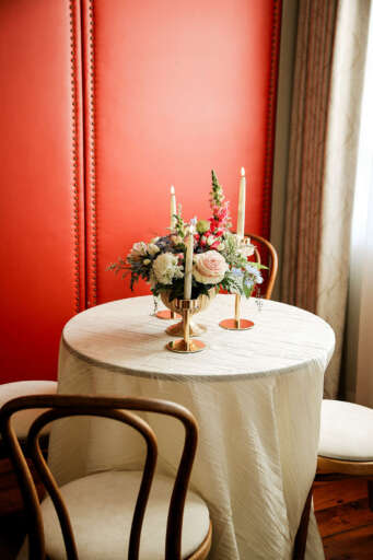 a round table with a white tablecloth, flowers, and candles in front of a red wall